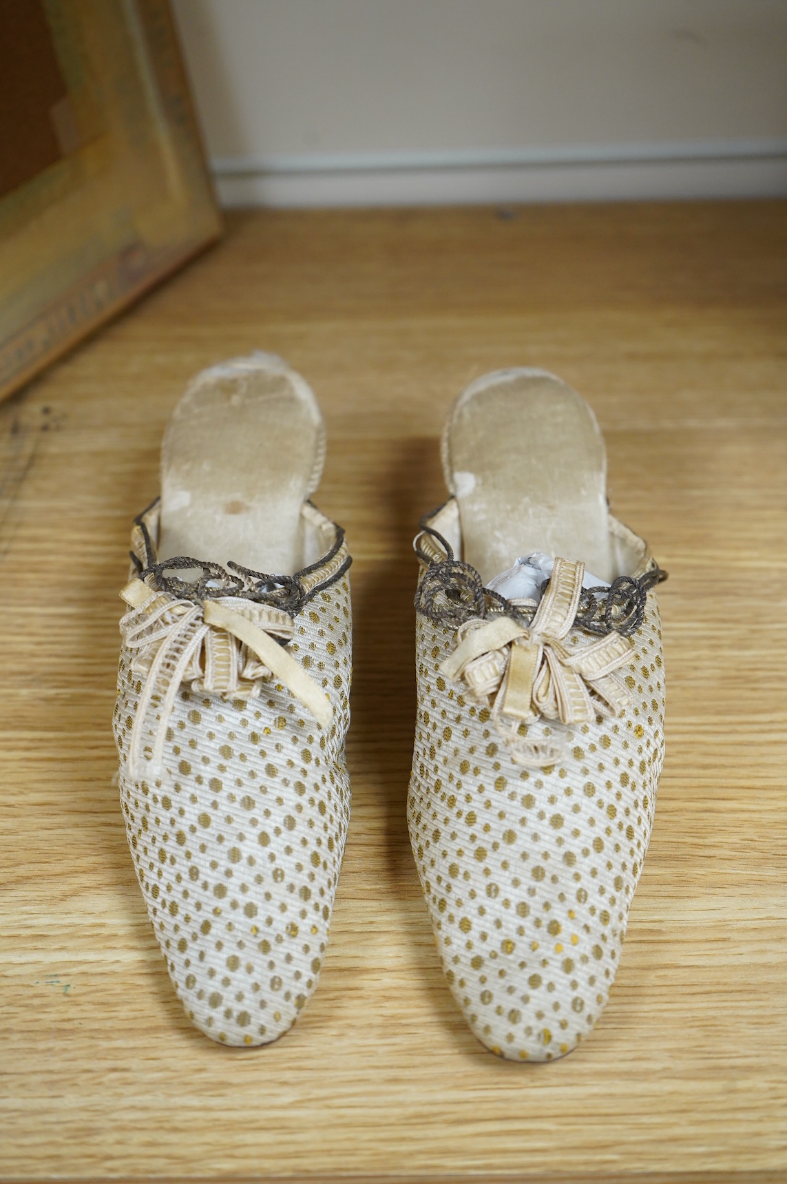 Of interest to collectors and costume designers: a pair of late 19th / early 20th century ladies gold spot embroidered mules, decorated at the front with a rosette of silk ribboning and fine cording. Condition - the cord